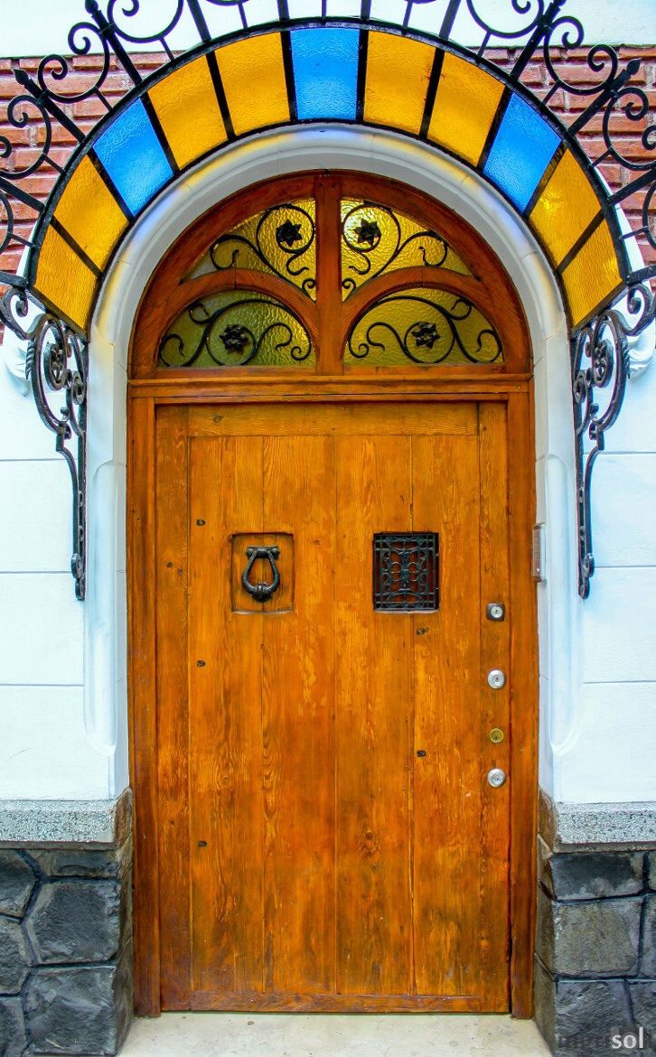 Широкая деревянная дверь, обрамленная кованным козырьком с цветным стеклом.